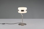 Lampa stołowa Dios z metalowym, niklowym stelażem. Okrągła, biała oprawa LED o mocy 8W z metalową obręczą. Ujęcie z boku, na płaskiej powierzchni z widocznym przewodem zasilającym. Tło w odcieniach szarości.