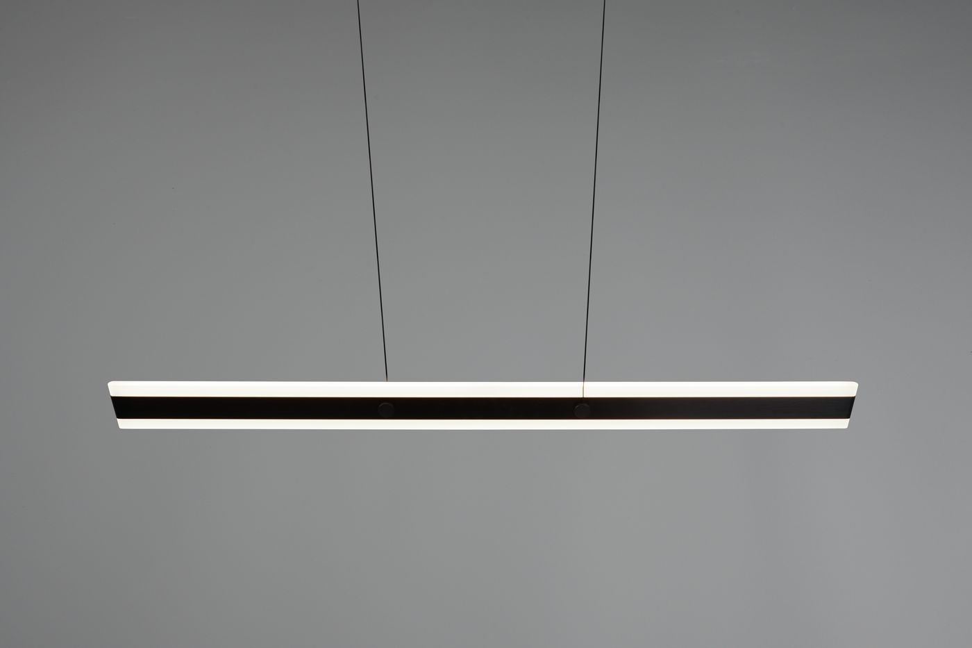 Czarna lampa wisząca Arcola z jedną diodą LED 35W CCT, w formie prostokątnej listwy. Zawieszona na cienkich linkach, z białą krawędzią, umieszczona na szarym tle. Idealna do nowoczesnych wnętrz.