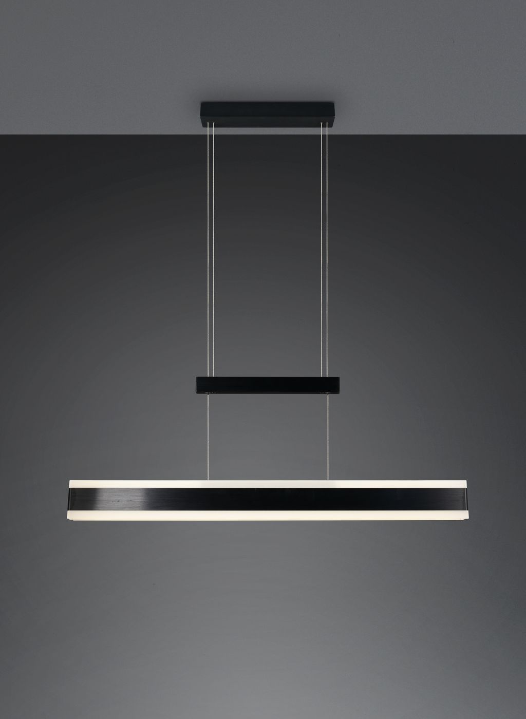 Lampa wisząca Arcola z jedną diodą LED 45W w kolorze czarnym. Prosta, prostokątna forma z metalowym wykończeniem. Powieszona na cienkich linkach, z górnym elementem montującym w czerni. Tło ciemne, podkreślające elegancki design.