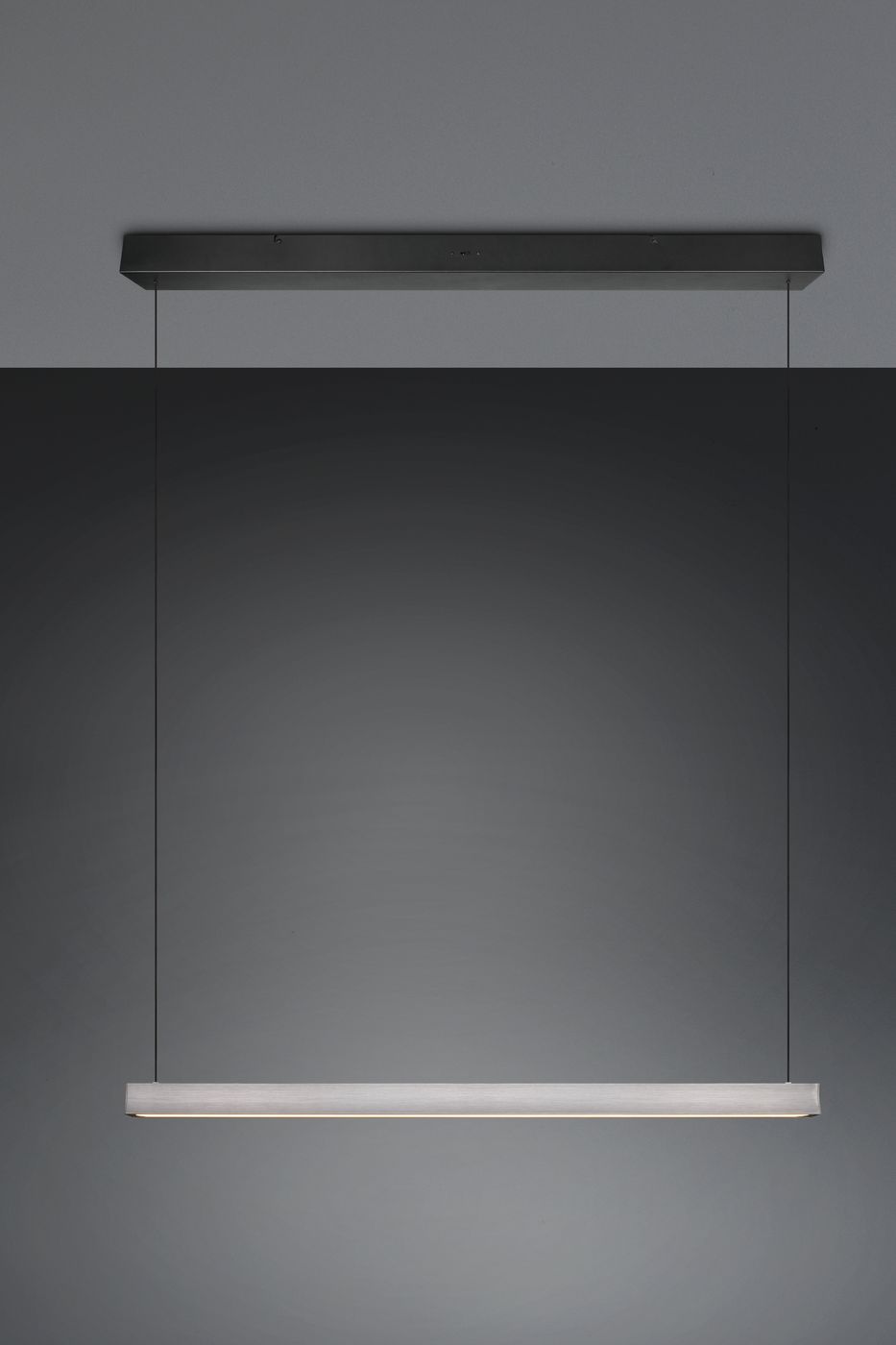 Lampa wisząca Wallace z jedną diodą LED 29W w kolorze czarnym i niklowym. Posiada prostokątny, smukły klosz z matowego materiału. Zawieszona na cienkich żyłkach, montowana na suficie, prezentuje nowoczesny design. Tło szare, minimalistyczne.