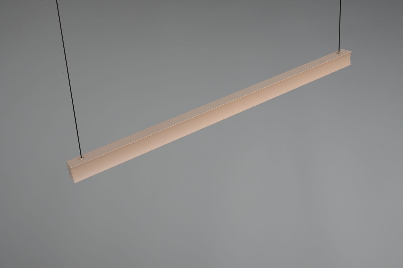 Beżowa lampa wisząca Wallace z jedną diodą LED o mocy 29W. Prosty, długi kształt, zawieszona na cienkich linkach, idealna do nowoczesnych wnętrz. Tło szare, podkreślające design lampy.