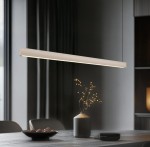 Lampa wisząca Wallace 1xLED 29W CCT w kolorze beżowym, w prostokątnym kształcie, zawieszona nad drewnianym stołem. W tle widoczny czarny talerz z czekoladkami oraz dekoracyjny wazon z gałązkami.