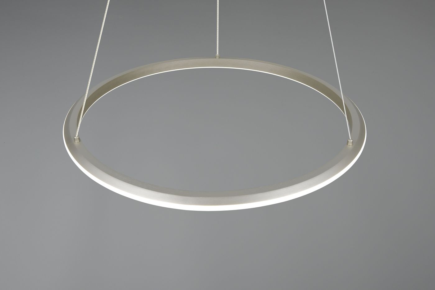 Lampa wisząca Amador w kształcie okręgu, wykonana z niklu, z jednym źródłem światła LED 48W CCT. Prezentowana z boku, zawieszona na cienkich żyłkach, na gładkim szarym tle.