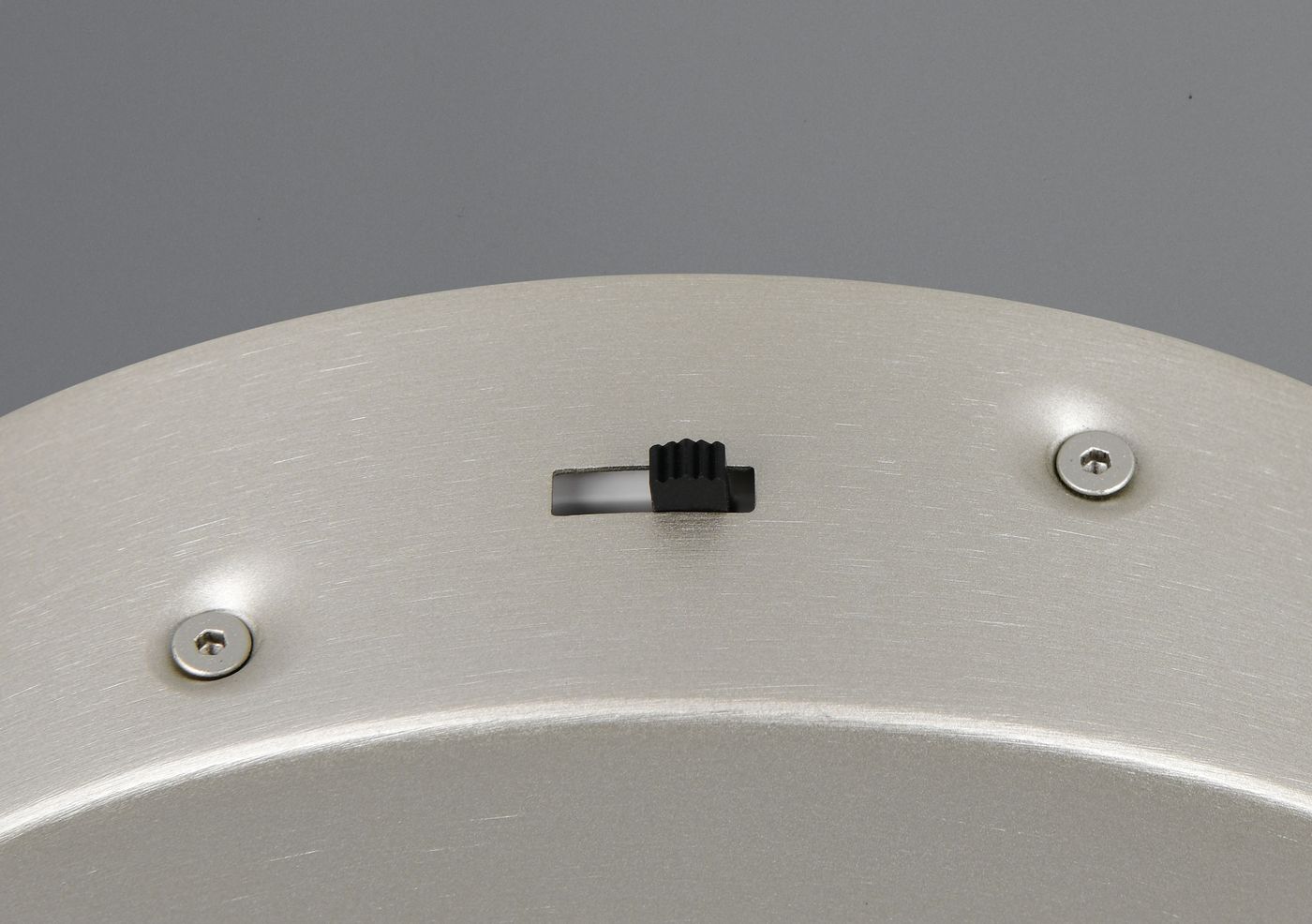 Lampa wisząca Amador w kolorze niklowym, z widocznym włącznikiem i metalowymi detalami. Ujęcie zbliżeniowe na górną część lampy, podkreślające fakturę materiału oraz elementy mocujące.