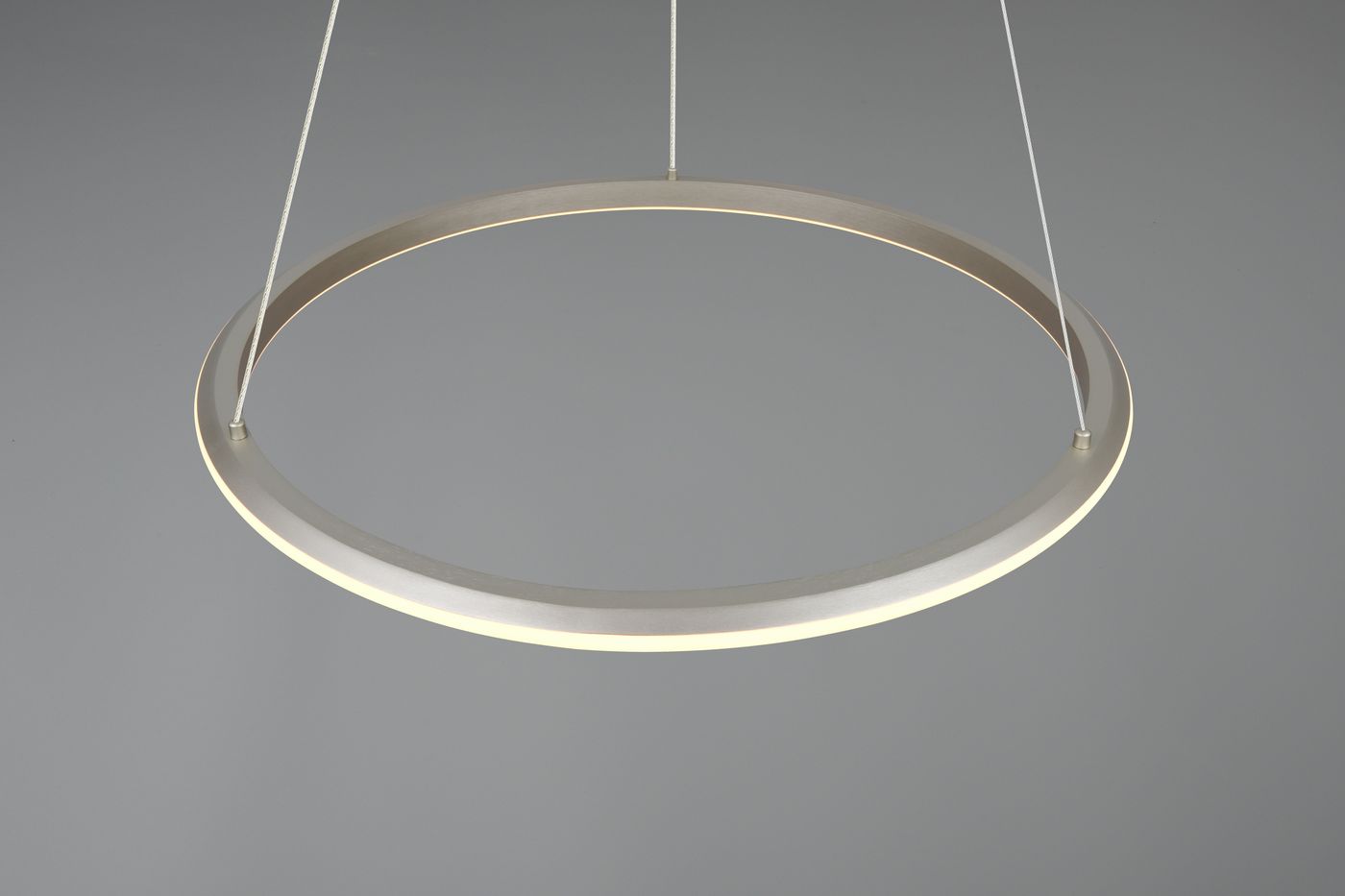 Lampa wisząca Amador w kolorze niklowym, o okrągłym kształcie, z wbudowanym oświetleniem LED 48W CCT. Zawieszona na cienkich linkach, emituje delikatne światło z krawędzi. Tło zdjęcia w szarości, co podkreśla minimalistyczny design lampy.