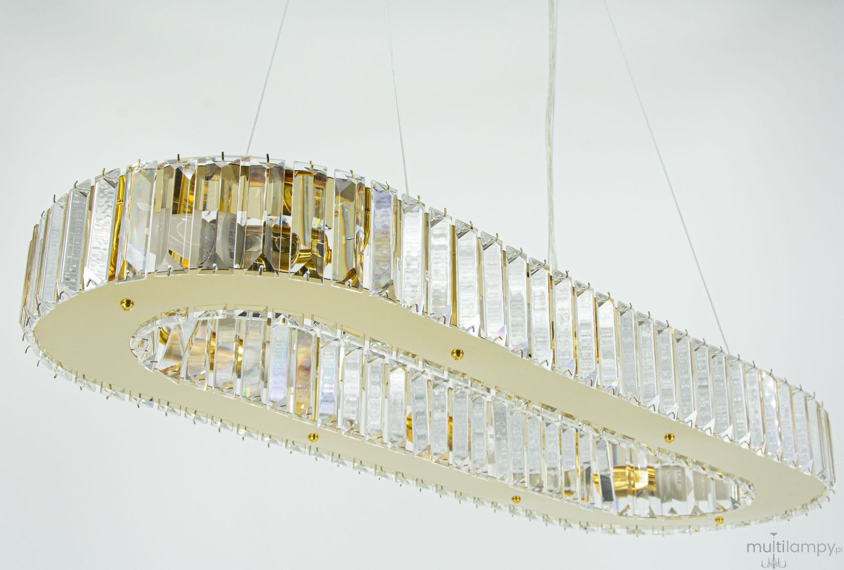 Lampa wisząca Windsor 8xE14 w kolorze złotym z przezroczystymi dekoracjami. Posiada owalny kształt z kryształowymi elementami, zawieszona na cienkich linkach. Widoczny detal w postaci złotych mocowań oraz błyszczących powierzchni.
