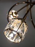 Lampa wisząca Aurora 3xE14 w kolorze złotym, z kryształowym kloszem. Widoczne elementy metalowe oraz połyskujące detale. Ujęcie zbliżeniowe na klosz z włączonym światłem, podkreślające fakturę i refleksy świetlne.