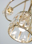 Lampa wisząca Aurora w kolorze złotym z trzema oprawkami E14. Elementy dekoracyjne z przezroczystego kryształu, o cylindrycznym kształcie, z metalową ramą. Widok zbliżeniowy na detale klosza oraz źródło światła.
