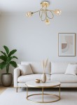 Lampa wisząca Aurora 3xE14 w kolorze złotym, z trzema kloszami w formie geometrycznych, szklanych elementów. Ujęcie z dołu, produkt zamontowany na suficie, w tle jasny pokój z sofą, rośliną i stolikiem kawowym.