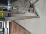Lampa wisząca Oxford 4-punktowa P04052NI z metalową, stalową ramą, szklanymi kloszami w formie cylindrów. Ujęcie z boku, ukazujące detale mocowania i przezroczystych elementów. Tło neutralne, z widocznymi książkami i pojemnikiem.