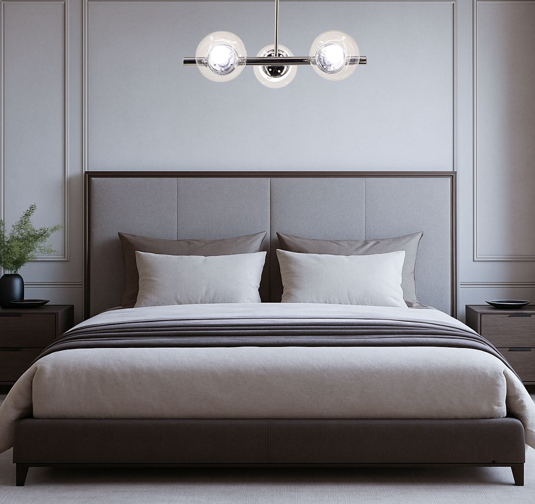 Lampa wisząca Otis 3xE27 w chromowanej obudowie, umieszczona nad łóżkiem w sypialni. Posiada trzy szklane klosze w kształcie kul, oświetlające przestrzeń. Tło stanowi jasna ściana z delikatnymi detalami, a meble są w odcieniach brązu.