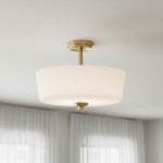 Lampa sufitowa Aspen 3xE27 w kolorze mosiądzu i białym abażurze, o okrągłym kształcie. Zawieszona na metalowym mocowaniu, widoczna z dołu, w jasnym wnętrzu z firanami. Idealna do nowoczesnych aranżacji.