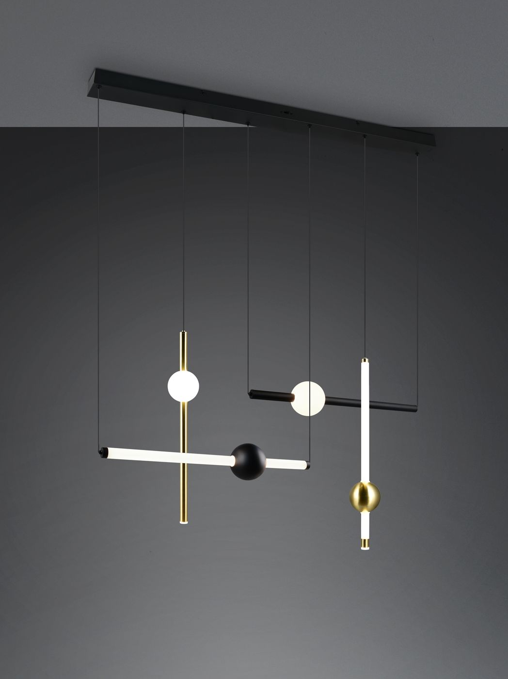 Lampa wisząca Melita z czterema źródłami LED 21W. Konstrukcja w odcieniach czerni i złota, z różnymi geometrycznymi kształtami, w tym cylindrycznymi i kulistymi, zawieszona na cienkich linkach. Tło szare, minimalistyczne.