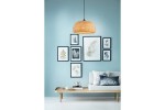 Lampa wisząca Sorell w kształcie półkuli, wykonana z czarnego rattanu, zawieszona na cienkim kablu. W tle niebieska ściana i galeria zdjęć w ramach. Mebel pod lampą to jasna sofa z poduszkami i drewniany stolik z filiżanką oraz książką.
