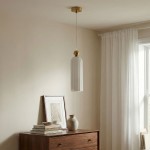 Lampa wisząca Piega 1-punktowa w kolorze patyny i białym, z cylindrycznym kloszem i złotym wykończeniem. Zawieszona pod sufitem, na tle jasnej ściany i drewnianej komody z książkami oraz wazonem.
