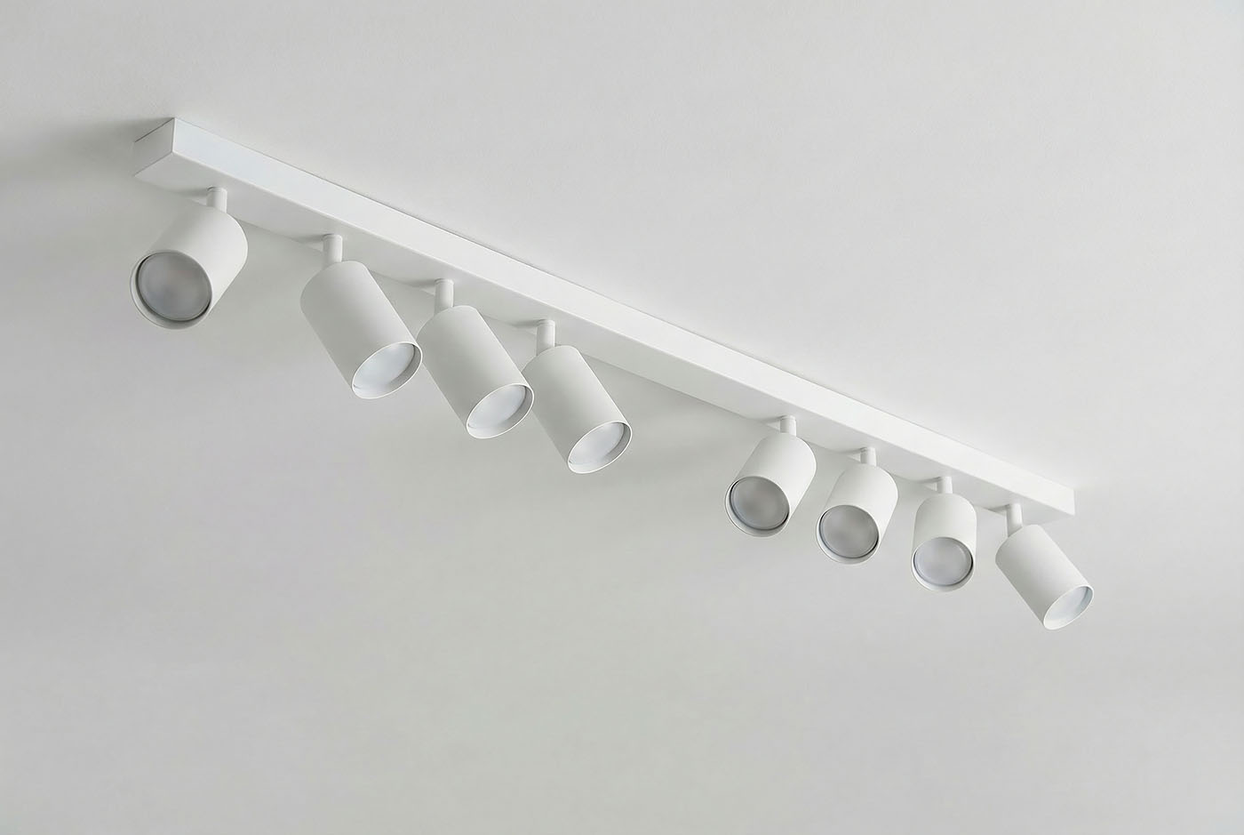 Biała lampa sufitowa (spot) z ośmioma regulowanymi punktami świetlnymi, zamontowana na prostokątnej belce. Ujęcie z góry, ukazujące kształt reflektorów i ich rozmieszczenie. Tło jasne, minimalistyczne.