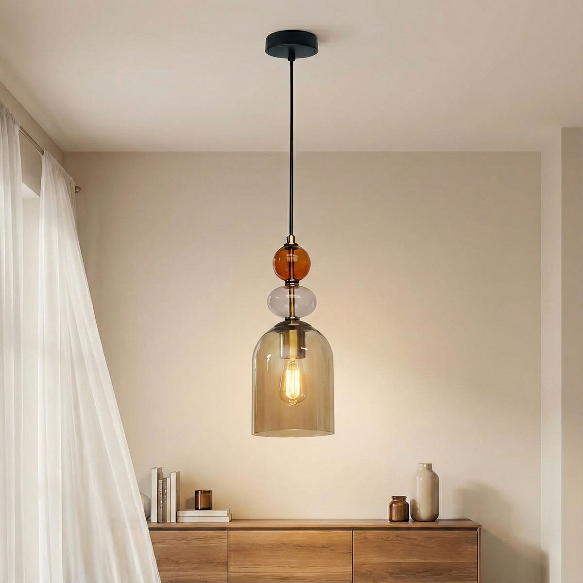 Czarna lampa wisząca Tropea z jedną oprawą E27. Szkło bursztynowe i przezroczyste tworzy efektowny klosz, zawieszony na cienkim, czarnym przewodzie. Lampa umieszczona w jasnym wnętrzu, na tle drewnianego mebla.