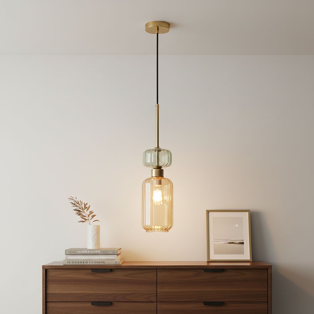 Lampa wisząca Molly z pojedynczym źródłem światła E14, w kolorze złotym i bursztynowym. Szklany klosz o cylindrycznym kształcie z dekoracyjnym elementem u góry. Zawieszona na czarnym przewodzie, umieszczona nad drewnianą komodą, we wnętrzu.