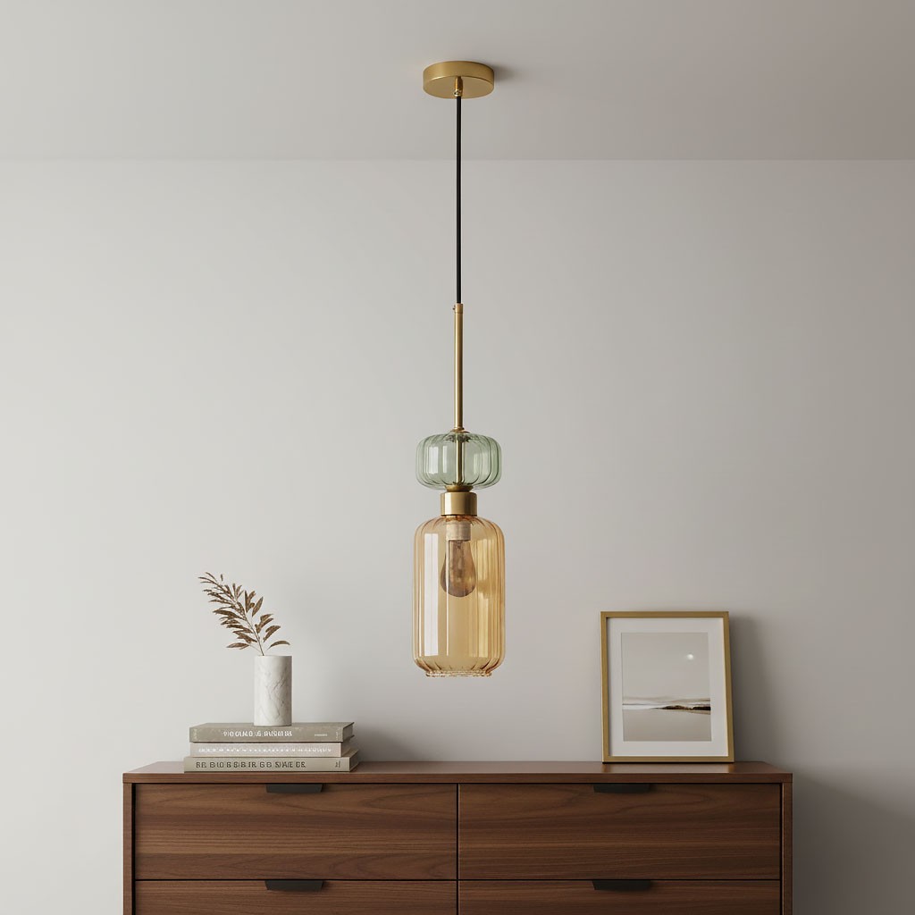 Lampa wisząca Molly z jedną oprawą E14, w kolorze złotym i bursztynowym, zawieszona na czarnym przewodzie. Posiada szklany klosz o bursztynowym odcieniu oraz dekoracyjny, zielony element u góry. W tle widoczna komoda z książkami i wazonem.