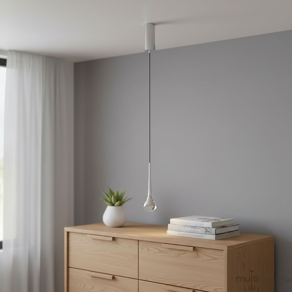 Lampa wisząca Crima Cromo LED w kształcie kropli, zawieszona na cienkim, metalowym kablu. Wykończenie w kolorze przezroczystym z chromowanym elementem mocującym. W tle komoda z drewnianymi szufladami oraz doniczka z rośliną.