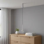 Lampa wisząca Crima Cromo LED w kształcie kropli, zawieszona na cienkim, metalowym kablu. Wykończenie w kolorze przezroczystym z chromowanym elementem mocującym. W tle komoda z drewnianymi szufladami oraz doniczka z rośliną.