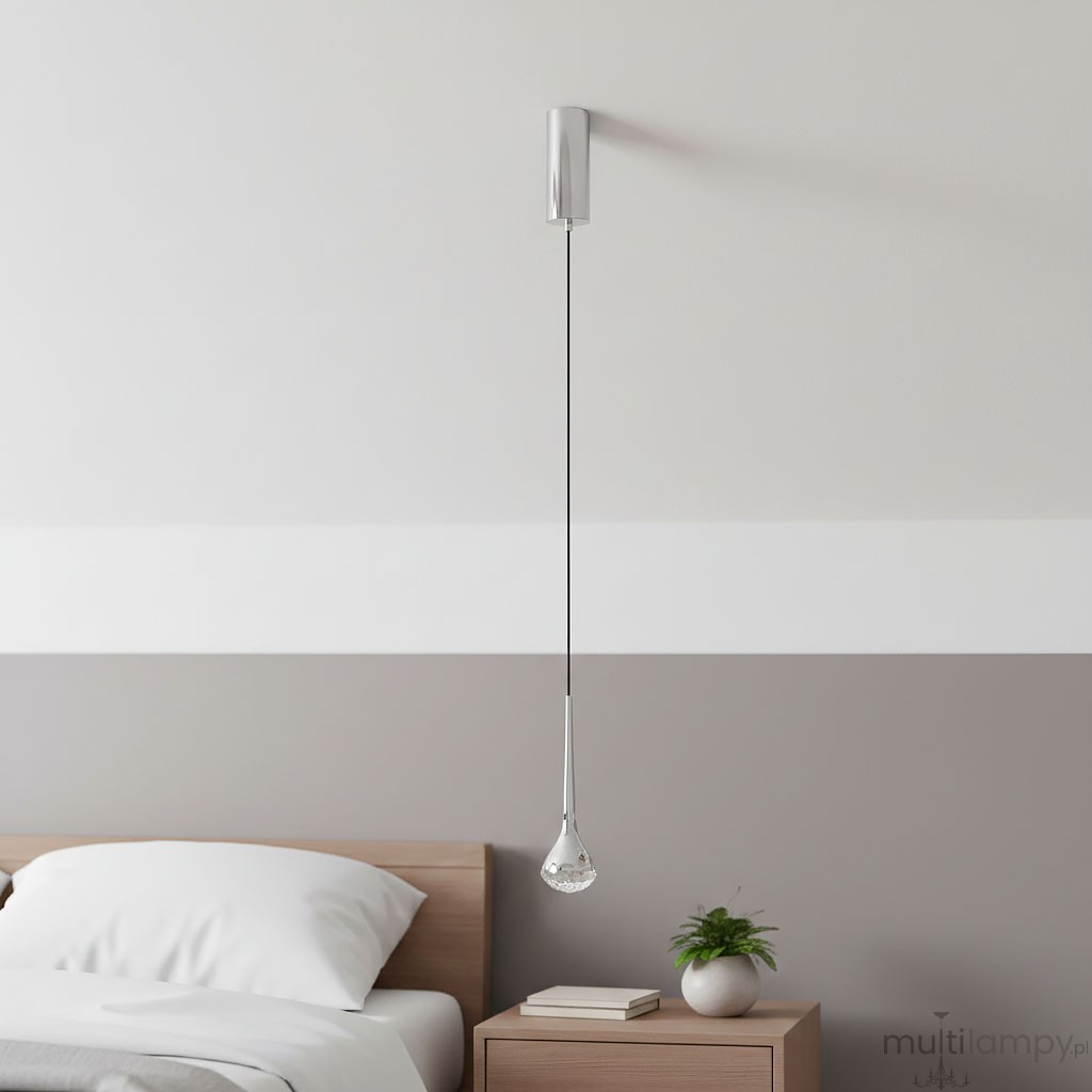 Lampa wisząca Crima Cromo LED w kształcie kropli, chromowane wykończenie, zawieszona na cienkim przewodzie. Umieszczona nad stolikiem nocnym w sypialni. Tło w odcieniach szarości i bieli, z widoczną rośliną doniczkową obok.