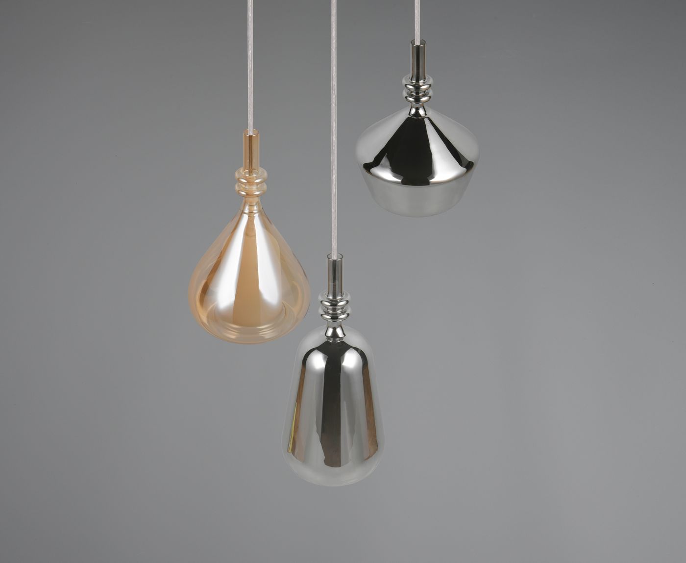 Lampa wisząca Aldea z trzema kloszami E14 w kształcie kropli, w kolorach złotym, srebrnym i białym. Klosze zawieszone na białych linkach, w neutralnym szarym tle, wiszą w różnych wysokościach, podkreślając nowoczesny design.