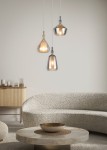 Lampa wisząca Aldea z trzema źródłami E14, w białym kolorze i multikolorowych kloszach. Ujęcie z przodu, z lampami w różnych kształtach: kropli, stożka i cylindrycznym. Produkt zawieszony nad okrągłym stołem na tle jasnej ściany.