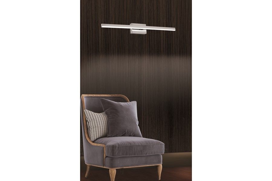 Kinkiet łazienkowy Linea L60 LED 8W 4000K IP44 w chromowanym wykończeniu, zamontowany na ciemnym tle, nad szarym fotelem. Lampa ma prostokątny kształt z elegancką, minimalistyczną konstrukcją.