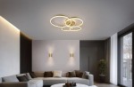 Lampa sufitowa Drake z pięcioma źródłami LED, 50W, w kolorze złotym. Posiada okrągłe, splątane elementy w nowoczesnym designie. Zawieszona na suficie w jasnym wnętrzu, otoczona meblami i dodatkami w neutralnych odcieniach.