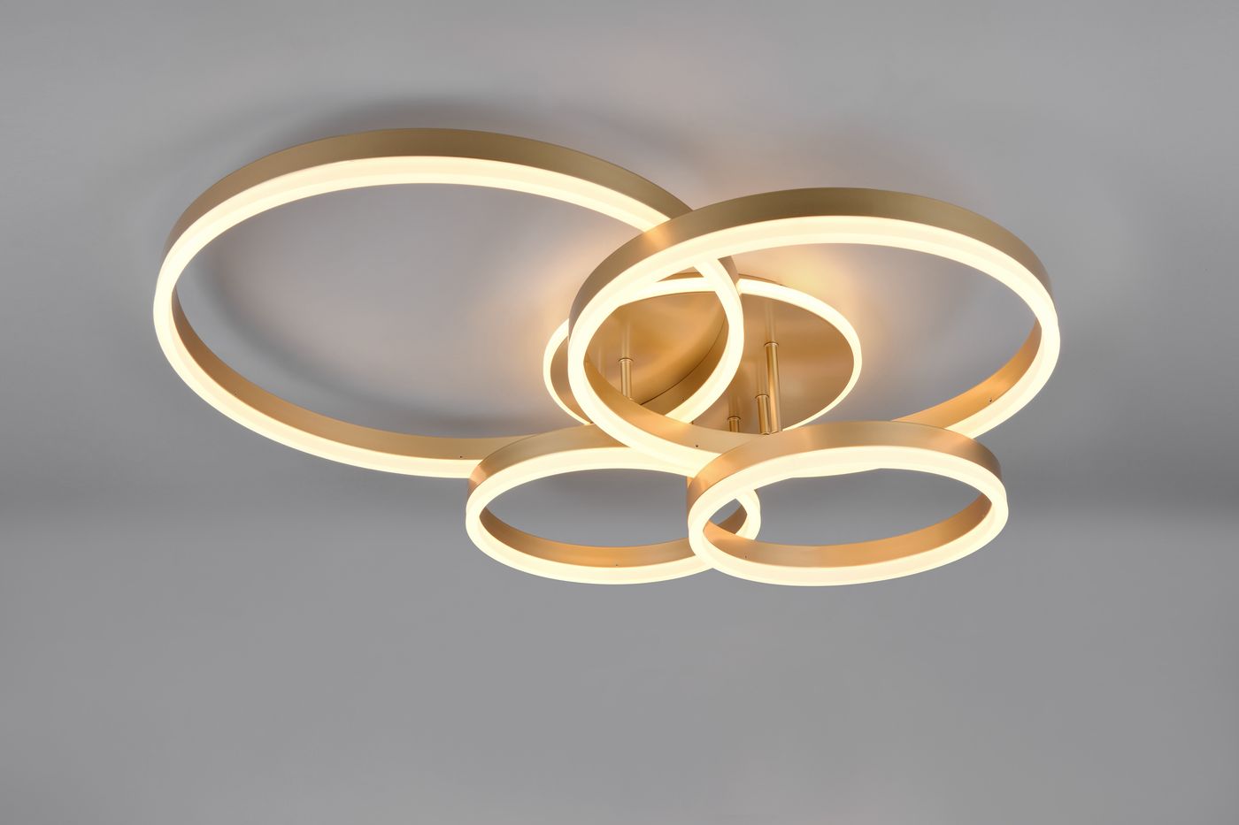 Lampa sufitowa Drake z pilotem, 5xLED/50W, w kolorze złotym. Składa się z trzech okrągłych pierścieni, zamontowanych na suficie, emitujących ciepłe światło. Kąt ujęcia z góry, na jednolitym tle.