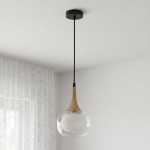 Czarna lampa wisząca Konila z mosiężnym detalem, zawieszona na cienkim przewodzie. Szklany klosz w kształcie kuli, transparentny, z białym wnętrzem. Lampa umieszczona w jasnym wnętrzu, z firanką w tle.