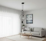 Lampa wisząca Trosti 2-punktowa w kolorze czarnym, z okrągłym elementem i białą kulą, zawieszona na dwóch czarnych przewodach. Produkt umieszczony w jasnym wnętrzu z szarym sofą i obrazem na ścianie.