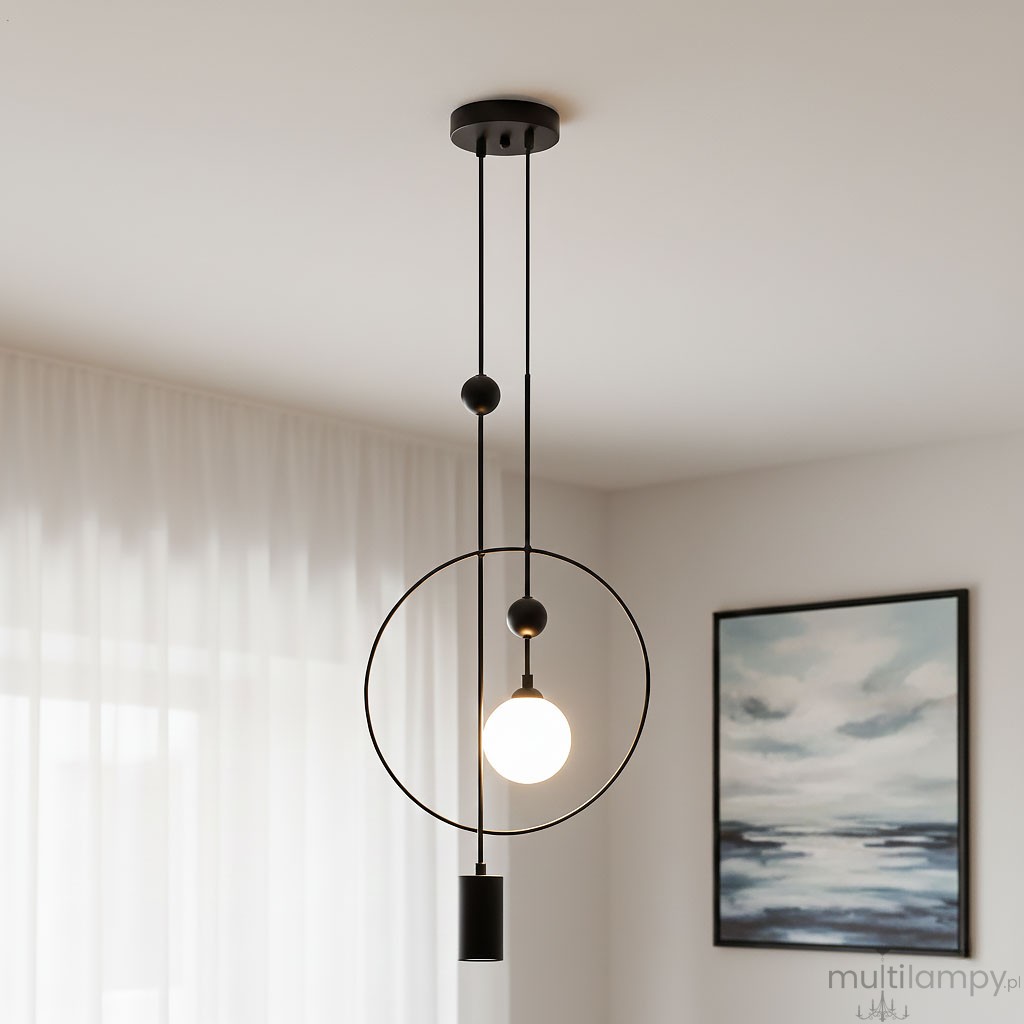 Lampa wisząca Trosti 2-punktowa w kolorze czarnym, z okrągłym ramieniem oraz przezroczystą kulą świetlną. Zawieszona na dwóch cienkich linkach, z dekoracyjnymi kulkami. Tło jasne, z zasłonami i obrazem w stonowanej kolorystyce.