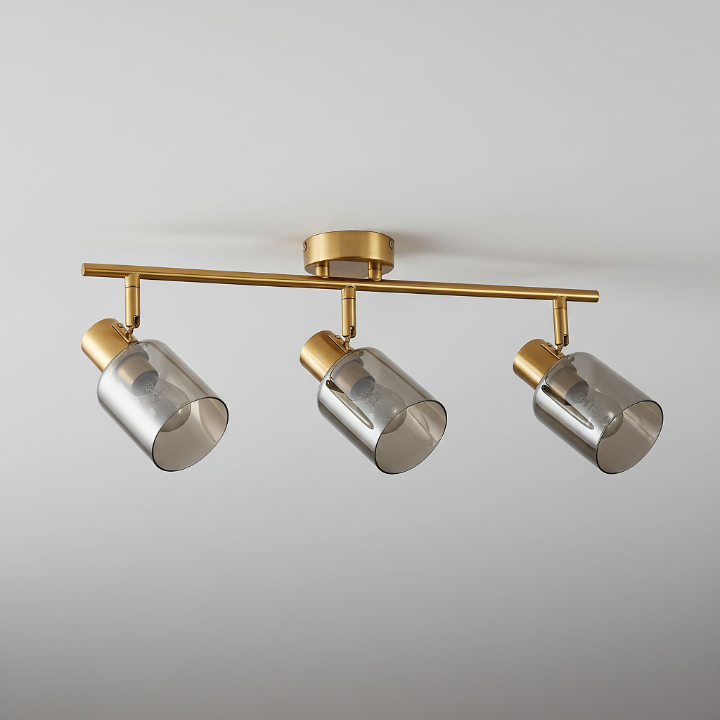 Lampa sufitowa Santia z trzema reflektorami E14, wykonana z mosiądzu i dymionego szkła. Reflektory mają cylindryczny kształt i są zamocowane na eleganckiej, złotej belce. Ujęcie frontalne, na jednolitym tle.