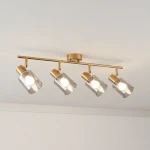 Lampa sufitowa Santia w kolorze mosiądzu z czterema szklanymi kloszami w dymionym odcieniu. Ułożona poziomo, z widocznymi źródłami światła E14. Klosze mają cylindryczny kształt, montaż na suficie. Tło jasne, minimalistyczne.