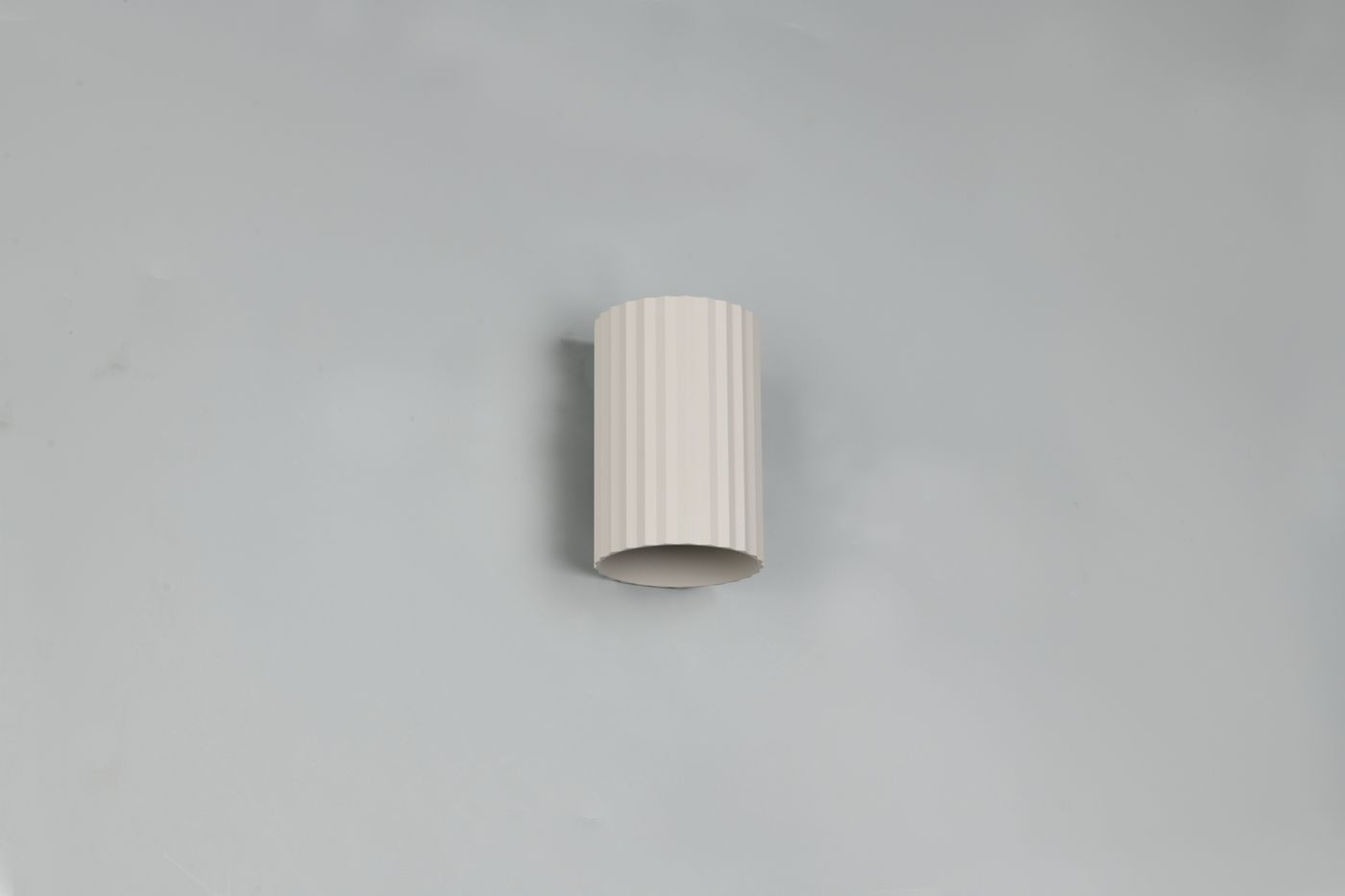 Kinkiet Imaria 1xG9 w kolorze szarym, o cylindrycznym kształcie z teksturowaną, żłobioną powierzchnią. Zamontowany na jasnej ścianie, prezentuje minimalistyczny design, idealny do nowoczesnych wnętrz.