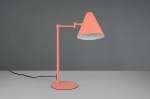 Lampa stołowa Cosima w kolorze morelowym z metalowym trzonkiem i stożkowym kloszem. Ujęcie frontalne, lampa stoi na okrągłej podstawie, z widoczną żarówką w środku. Kabel zasilający leży na stole, w tle szare ściany.