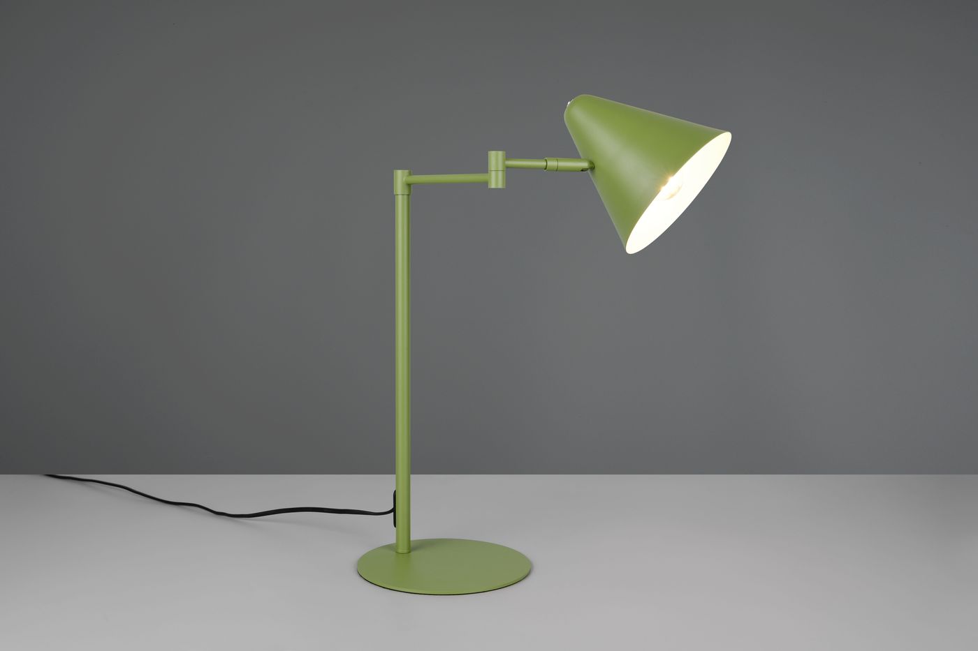 Zielona lampa stołowa z metalowym korpusem, z kloszem w kształcie stożka. Ujęcie z boku, stojąca na okrągłej podstawie. Widoczny przewód zasilający. Klosz skierowany w górę, podkreślający minimalistyczny design.