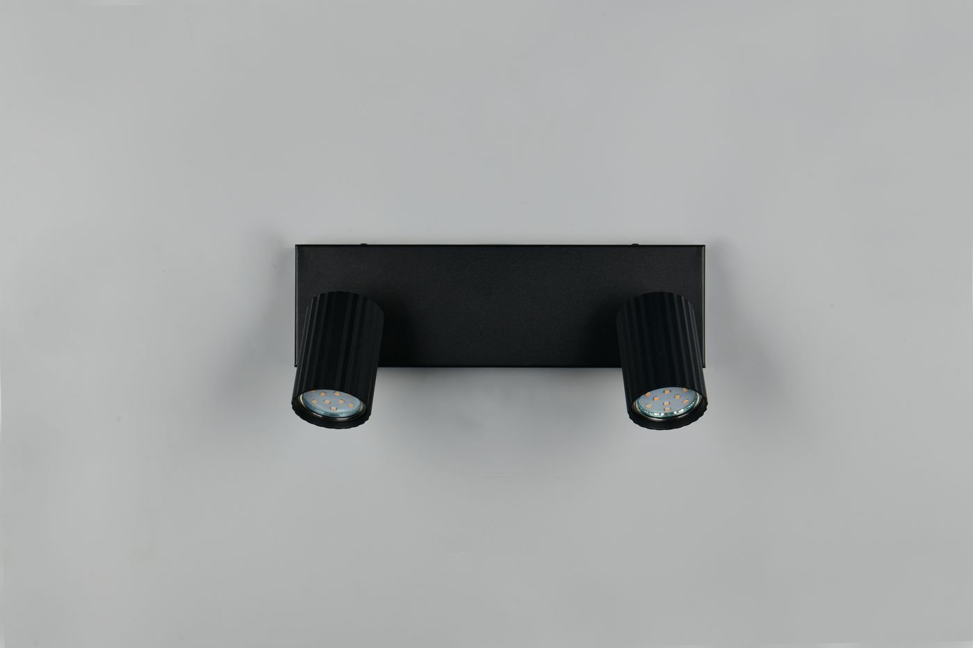 Czarna lampa sufitowa Soka z dwoma reflektorami GU10, zamontowana na prostokątnej podstawie. Reflektory mają żebrowaną fakturę i emitują światło z okrągłych kloszy. Produkt widoczny na szarym tle.