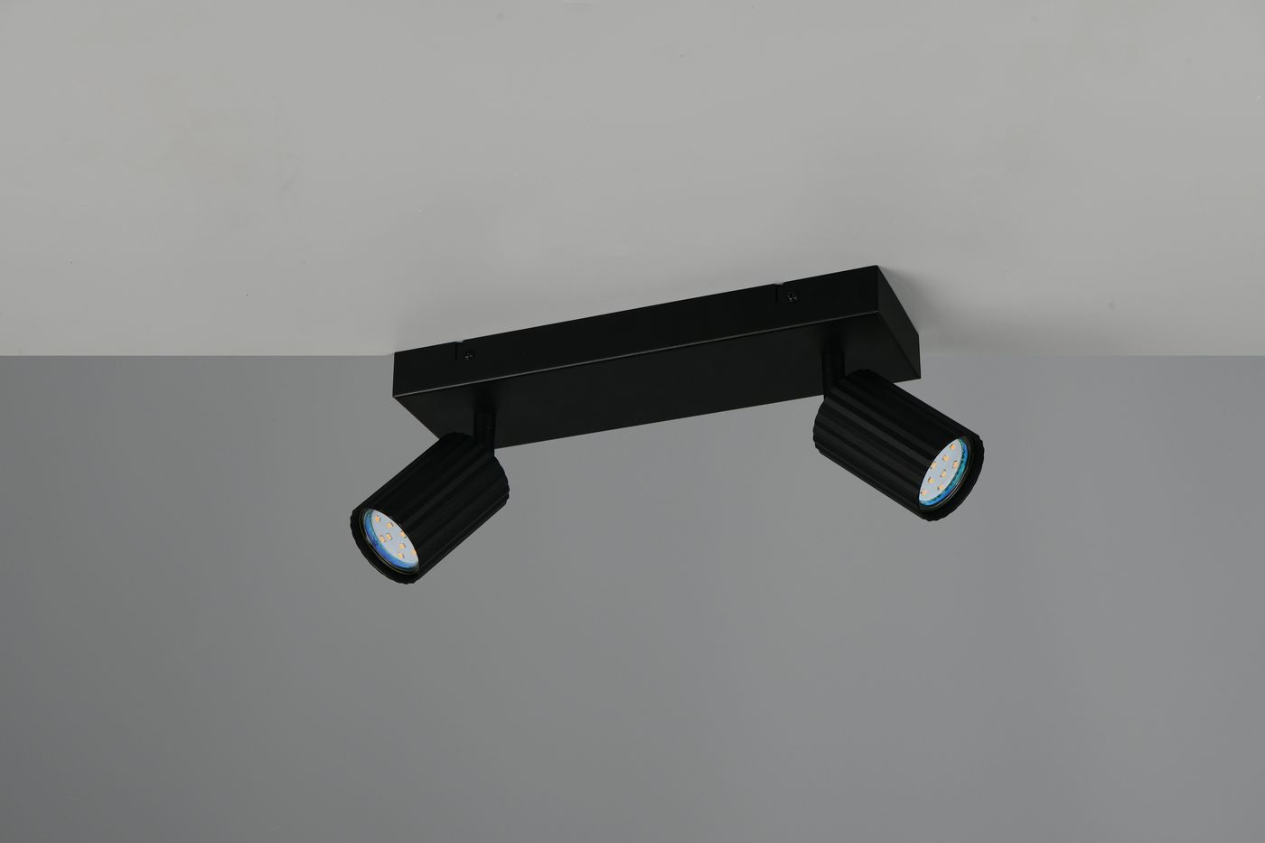 Czarna lampa sufitowa Soka z dwoma reflektorami GU10, umieszczona na prostokątnej podstawie. Reflektory mają teksturowaną powierzchnię i są skierowane w różne strony, co pozwala na regulację kierunku światła. Produkt zamontowany na gładkim, jasnym tle.