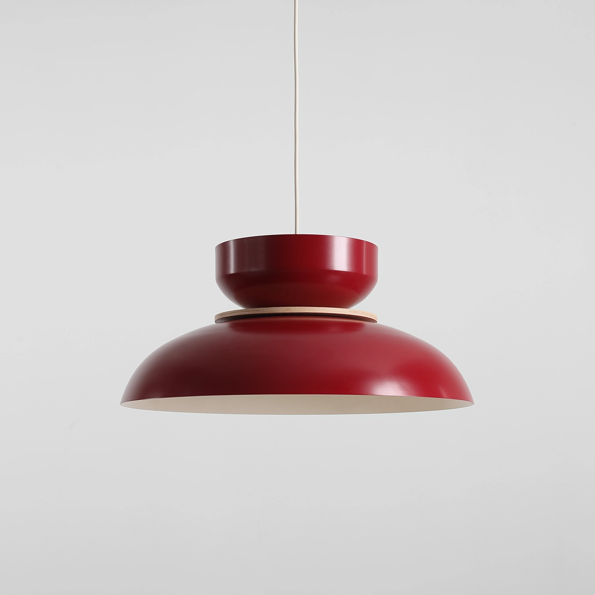 Lampa wisząca Aldo w kolorze czerwonego wina z jednym gniazdem E27. Okrągła, matowa czasza z szerokim brzegiem i ozdobnym, cylindrycznym uchwytem. Zawieszona na cienkim, białym przewodzie. Proste tło podkreśla elegancki design lampy.