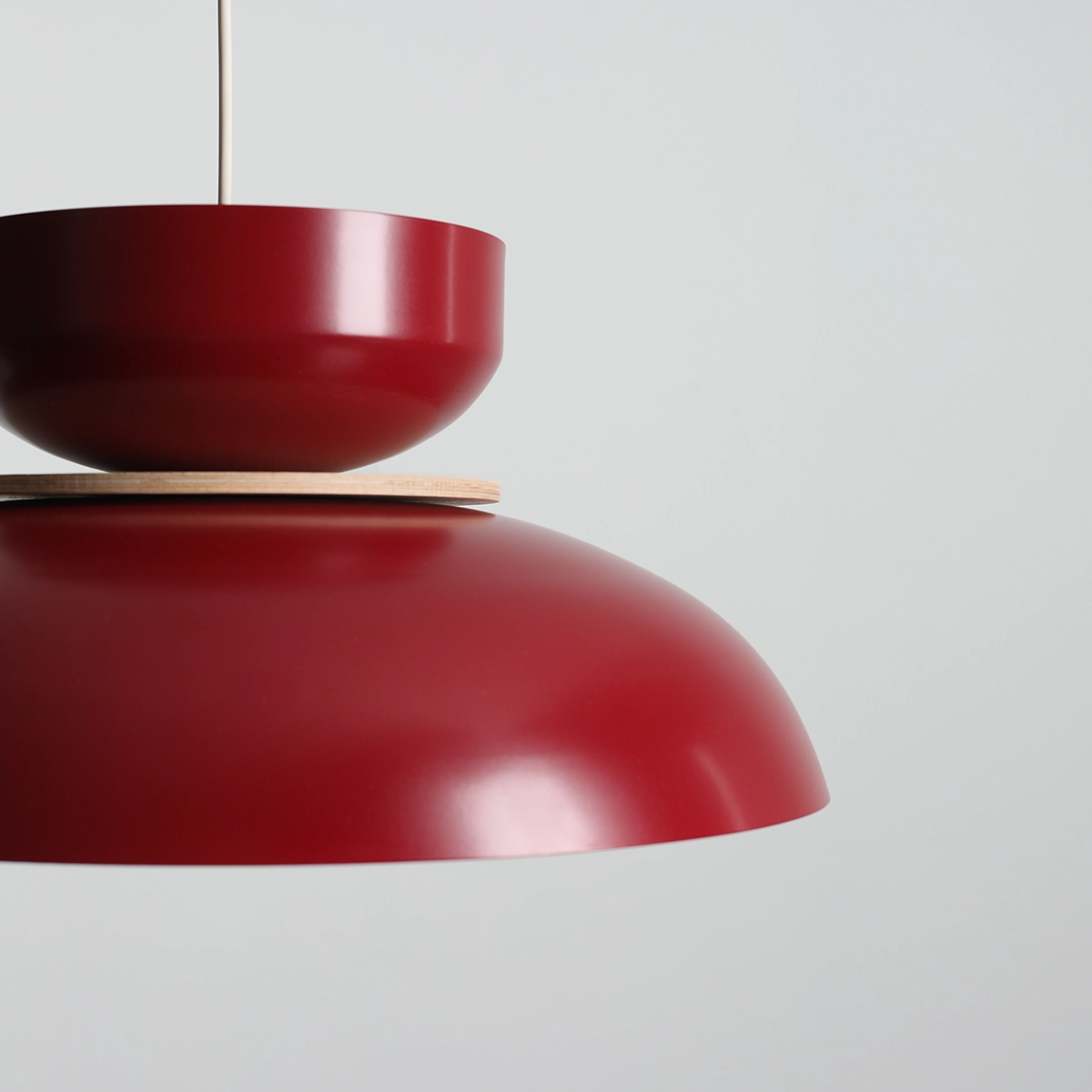 Lampa wisząca Aldo w kolorze czerwonego wina z metalowym kloszem o zaokrąglonym kształcie, z górną, mniejszą misą i drewnianym detalem. Ujęcie z boku, ukazujące detale konstrukcji. Tło jasne, neutralne.