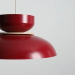 Lampa wisząca Aldo w kolorze czerwonego wina z metalowym kloszem o zaokrąglonym kształcie, z górną, mniejszą misą i drewnianym detalem. Ujęcie z boku, ukazujące detale konstrukcji. Tło jasne, neutralne.