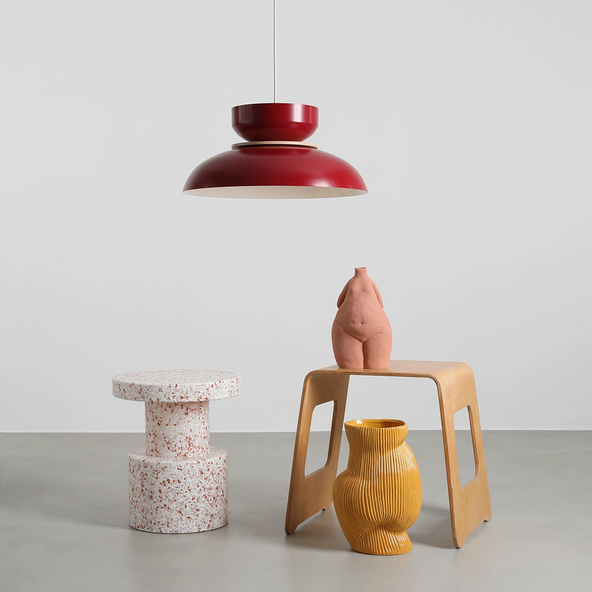 Lampa wisząca Aldo w kolorze czerwonego wina z jednym gniazdem E27, o okrągłym, matowym kloszu. Zawieszona nad drewnianym stołem, otoczona ceramicznymi dekoracjami w ciepłych kolorach. Tło jasne, minimalistyczne.