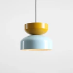 Lampa wisząca Tula z jedną oprawą E27 w kolorze błękitnym i musztardowym. Składa się z dwóch elementów o zaokrąglonym kształcie, umieszczonych jeden na drugim. Zawieszona na czarnym przewodzie, na prostym, jasnym tle.
