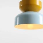 Lampa wisząca Tula 1xE27 w kolorze błękitnym i musztardowym, o okrągłym kształcie. Górna część w kolorze musztardowym, dolna błękitna z wewnętrzną, jasną powierzchnią. Ujęcie z bliska, pokazujące detale i fakturę materiału.