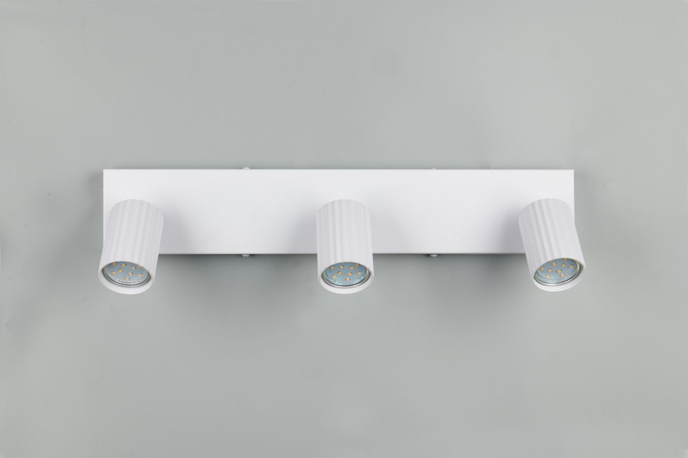 Lampa sufitowa Soka z trzema reflektorami GU10, w białym kolorze. Ułożona poziomo na prostokątnej podstawie, z cylindrycznymi kloszami o teksturowanej powierzchni, skierowanymi w różnych kierunkach. Tło szare.