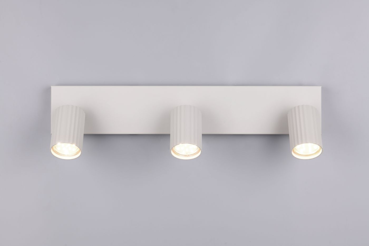 Szara lampa sufitowa Soka z trzema reflektorami GU10. Reflektory w cylindrycznych, żłobkowanych obudowach, zamontowane na prostokątnej bazie. Ujęcie frontalne, na jednolitym tle, podświetlenie widoczne. Idealna do nowoczesnych wnętrz.