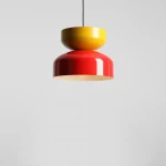 Lampa wisząca Tula z jednym gniazdem E27 w kolorach czerwonym chili i musztardowym. Okrągła, błyszcząca konstrukcja z górnym, żółtym kloszem oraz dolnym, czerwonym kloszem, zawieszona na czarnym przewodzie. Tło jasnoszare.